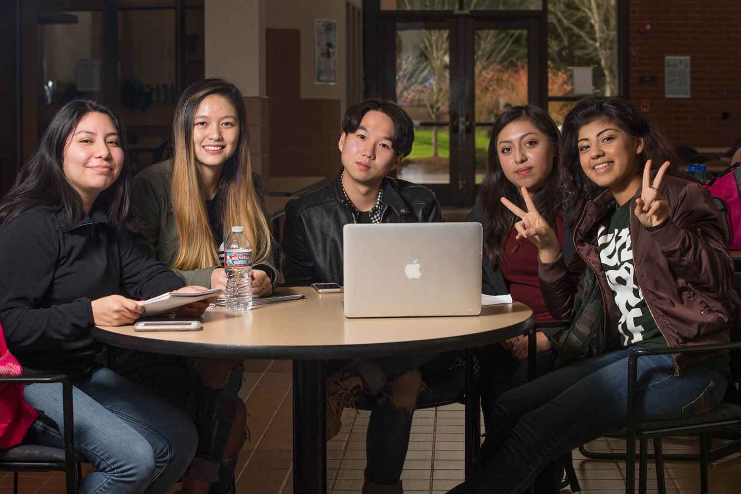 Five students gathered at a computer look up to say hello